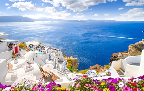 View through an open window with shutters of the whitewashed village of Oia rising above the blue Aegean Sea and the caldera on the island of Santorini, Greece. View through an open window with shutters of the whitewashed village of Oia rising above the blue Aegean Sea and the caldera on the island of Santorini, Greece.
