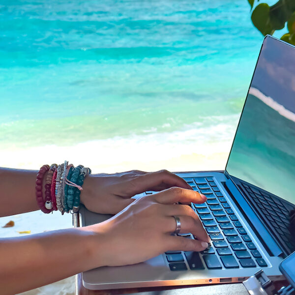 Nomad digital with laptop and running remotely with bright scenic view near poolside on the beach in summer time